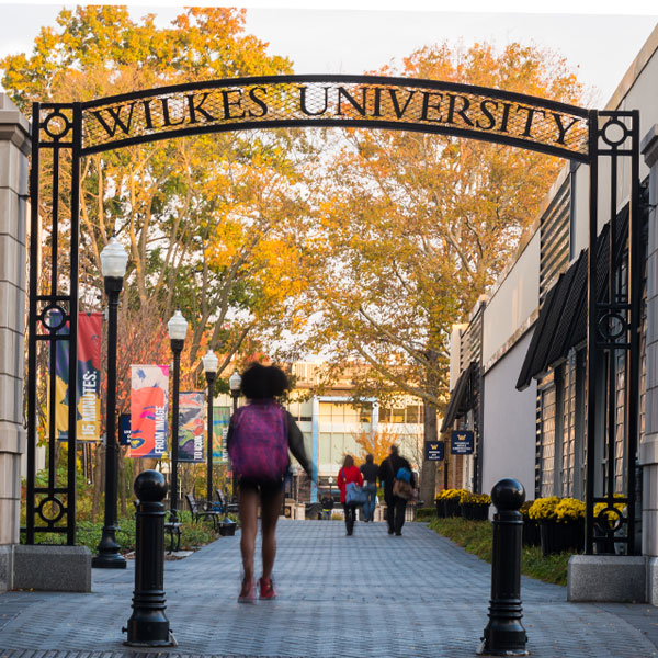 Wilkes student walking under campus gateway
